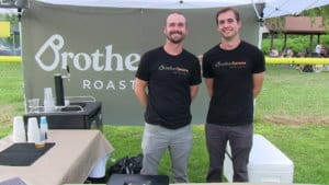 two men wearing brothers beans roasting shirts at a coffee vendor tent at a festival
